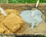 Brouette contenant du sable et du ciment, prêts pour le dosage béton. Une pelle est dans le sable, une truelle dans le ciment.