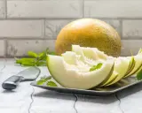 Kawałki melona na talerzu, obok cały owoc i nóż. Niska wartość melon indeks glikemiczny.