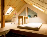 Un grenier en cours d'aménagement, avec isolation, un velux, une échelle et des plaques de plâtre.