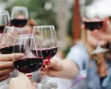 Des mains portent des verres de vin rouge pour un apéro convivial.