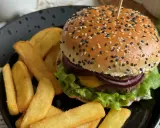 Soczysty burger wołowy z frytkami na czarnym talerzu.
