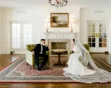 Para młoda w eleganckich strojach, symbolizująca małżeństwo cywilne, siedzi naprzeciwko siebie w przytulnym salonie.