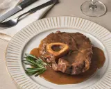 Un delicioso osso buco, tierno y jugoso, bañado en su salsa, servido en un plato con romero fresco.