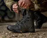 Mężczyzna w mundurze maskującym sznuruje czarne buty taktyczne. Gotowy na każde wyzwanie, te buty WOT zapewnią komfort i bezpieczeństwo.