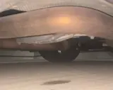 Mancha de líquido bajo el coche, indicando posible perdida de agua. Se ven tubos de escape y rueda.