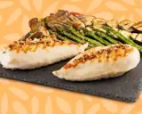 Dos jugosas pechugas de pollo a la parrilla, sazonadas con especias, acompañadas de espárragos, calabacín y champiñones.