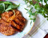 Grillowane plastry schabu w aromatycznej marynacie, podane z zielonymi liśćmi na talerzu.