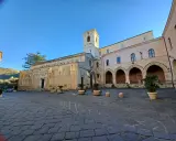 La piazza antistante la chiesa di Tropea, con il suo campanile e gli archi del chiostro, sotto un cielo azzurro.
