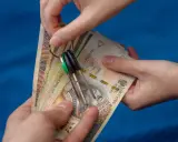 Dwie ręce trzymają plik banknotów i klucze. Zastanawiasz się, od jakiej kwoty płaci się podatek od wynajmu mieszkania?