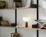 En stilren hylla i vardagsrummet med böcker, en vas och en lampa.