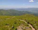 Malownicze widoki na Beskid Śląski, gdzie liczne istebne szlaki turystyczne prowadzą przez zielone wzgórza pełne jagód. Ludzie odpoczywają na trawie, ciesząc się słońcem.