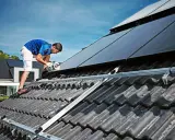 Handwerker montiert Solarmodule auf einem Dach. Dies geschieht unter Beachtung der hausanschluss strom vorschriften für eine sichere Installation.