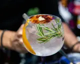 Ein erfrischender Gin Tonic, ein klassischer Cocktail, garniert mit Rosmarin, Orangenzeste und karamellisiertem Zucker.