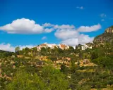 Pueblo blanco en la ladera de una montaña, rodeado de olivos y vegetación. El cielo azul con nubes blancas corona la vista de Gontar, Albacete.