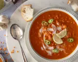 Eine cremige rote Linsensuppe mit Kokosmilch, garniert mit Limettenspalten und Jalapeños. Dazu gibt es knuspriges Brot.