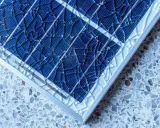 Gros plan sur un vitre panneau solaire brisé, ses fragments bleus reflétant la lumière sur un fond moucheté.