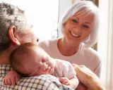 Los abuelos paternos sonríen mientras el abuelo sostiene al bebé dormido en su hombro.