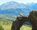 Arco natural en el valle de Tena, con vistas a montañas y un pueblo. Imagina a niños explorando este paisaje.