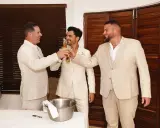 Tres hombres en trajes claros brindan con cerveza. El novio, en el centro, sonríe. Un momento de alegría antes del discurso de boda hermano.