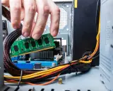Main d'un homme insérant une barrette de RAM verte dans un emplacement de carte mère. Guide pour comment installer RAM.