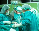 Zespół chirurgów w zielonych fartuchach i czepkach przeprowadza skomplikowaną operację głosu.