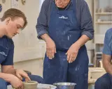 En ung man lär sig tumning keramik på en kurs. En äldre man och en kvinna tittar på.