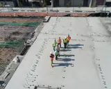 Grupa budowlańców na placu budowy, gdzie trwa wylewanie betonu. Zastanawiają się, ile kosztuje gruszka betonu, analizując postęp prac.