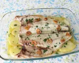Lubina a la espalda horneada con patatas, ajo y perejil en una fuente de cristal.