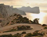Kręta droga prowadzi do Playa de Formentor, otoczona skalistymi zboczami i morzem o zachodzie słońca.
