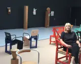 En kvinna sitter i en röd stol i en utställning med möbler av John Kandell.