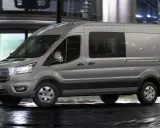 Camión N1 gris Ford Transit circulando por una calle urbana mojada de noche, con luces de edificios y tráfico difuminadas al fondo.