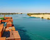 Containerrieschiff fährt durch den Suezkanal, ein Meisterwerk des Suezkanal Baus, vorbei an Wüstenlandschaft und Stadt.