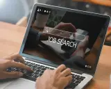 Ręce wpisują "JOB SEARCH" na laptopie. Praca wre, szukamy nowych możliwości.