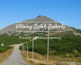 Kamienista ścieżka prowadzi na szczyt góry, gdzie widać budynek. Nad krajobrazem widnieje napis "Główny Szlak Sudecki".