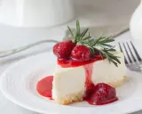 Ein Stück cremige Philadelphia Torte mit Erdbeersauce und frischen Erdbeeren, garniert mit Rosmarin.