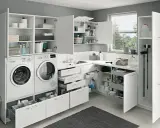 Ein heller, moderner kleiner Hauswirtschaftsraum mit Waschmaschine, Trockner, Spüle und viel Stauraum in weißen Schränken.
