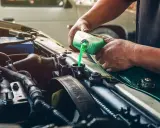 Mecánico rellenando refrigerante verde en el radiador de un coche, solucionando una posible fuga de gas aire acondicionado.