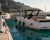 Un catamaran électrique blanc est amarré à quai, branché à une borne de recharge. Le port est bordé de collines verdoyantes.