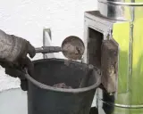 Rękawica z łopatką usuwa sadzę z komina do wiadra. Czyszczenie komina od dołu to ważny etap dbania o bezpieczeństwo.