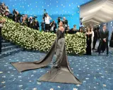Kylie Jenner arrives at the Met Gala in a dramatic gown, posing for photographers amidst a sea of flowers and a blue, star-studded backdrop.