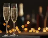 Zwei Sektgläser mit sprudelndem Sekt, im Hintergrund unscharfe Flaschen und Lichter. Ein krug 169 für besondere Anlässe.