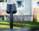 Svart laddstolpe Easee med krokar för laddkablar, placerad utomhus framför ett bostadshus.