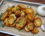 Knusprige Kartoffelscheiben aus dem Airfryer, garniert mit Petersilie, daneben Rosmarin, Knoblauch und eine ganze Knoblauchknolle.