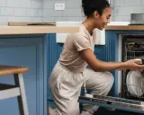 Une femme charge son lave-vaisselle encastrable. Elle place une casserole dans le panier inférieur.