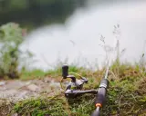 Wędka i kołowrotek leżą na trawie nad wodą.