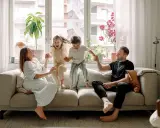 Familjen hoppar glatt på soffan i detta hemma hos reportage. Barnen skrattar högt medan föräldrarna ler.