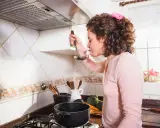 Kobieta w kuchni, zastanawia się, jak wyczyścić kratkę okapu. Na blacie stoją warzywa i garnki.