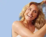 Uśmiechnięta blondynka aplikuje puder do włosów z żółtej buteleczki na swoje kosmyki.