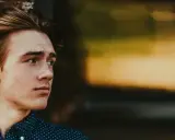 Junger Mann mit stylischen herren frisuren mittellang, lehnt an einer Ziegelwand.