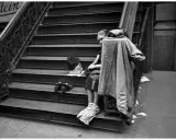 Una persona seduta sulle scale, con scarpe e cappello accanto. Un'immagine che evoca le cartier bresson foto famose, catturando un momento di vita urbana.